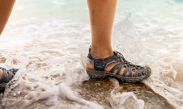 Woman walking along ocean rocks in Keen sandals