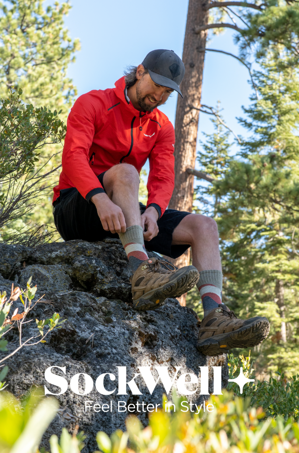 Man pulling up sock while sitting on rock