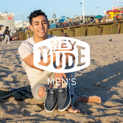 Man sitting in sand holding shoes