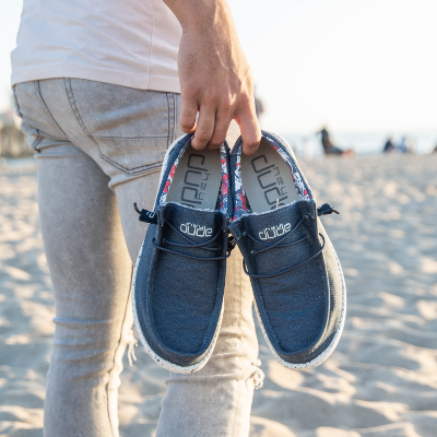 Man holding shoes in hand, walking on beach
