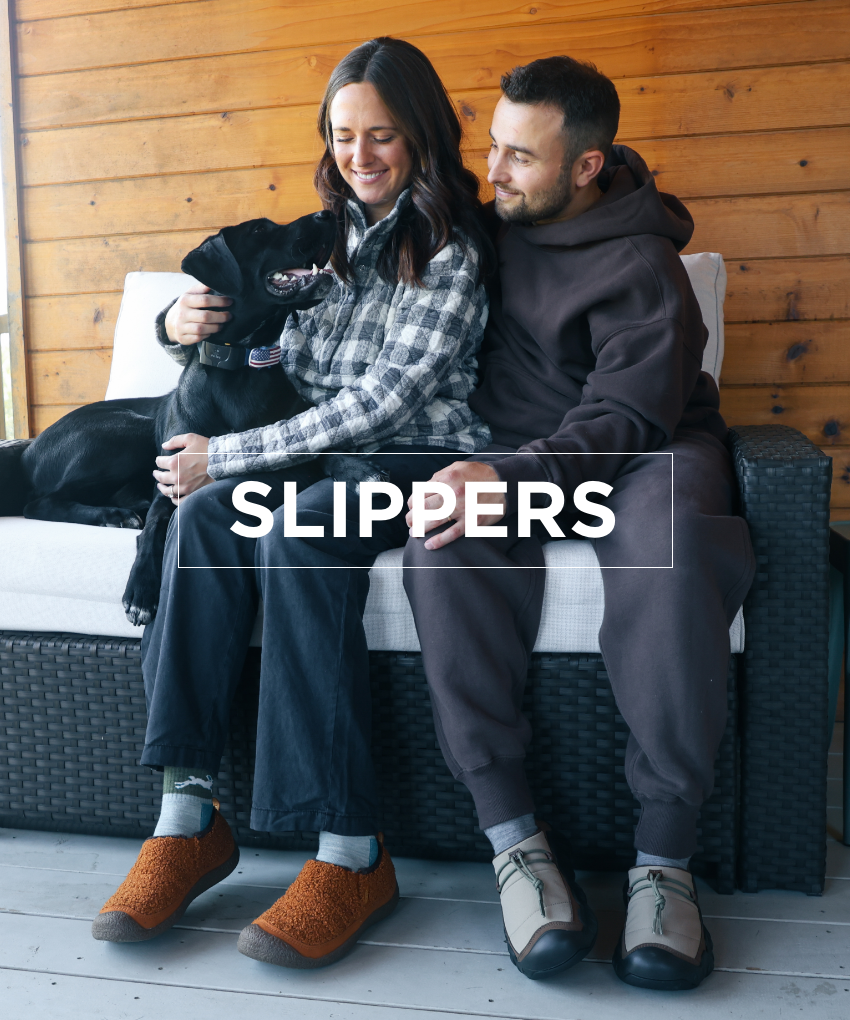 Man and woman cuddling dog on couch wearing Keen slippers
