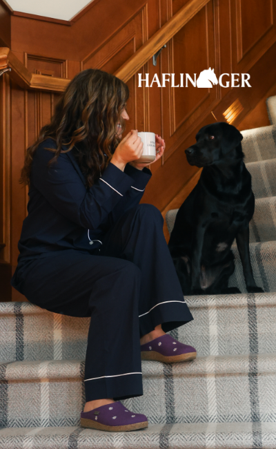 Woman sitting on stairs petting dog wearing Haflinger Grizzly Margherita slippers
