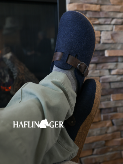Man crossing feet in chair wearing Haflinger Grizzly Buckle Slippers