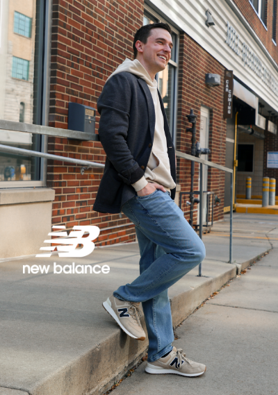 Man leaning against railing downtown wearing New Balance 574 lifestyle sneakers