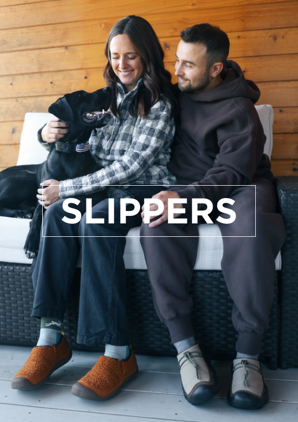 Man and woman cuddling dog on couch in Keen slippers