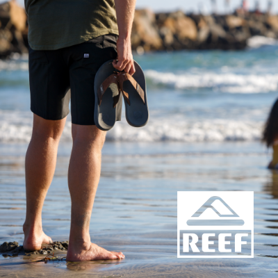 Man holding sandals in hand by ocean 